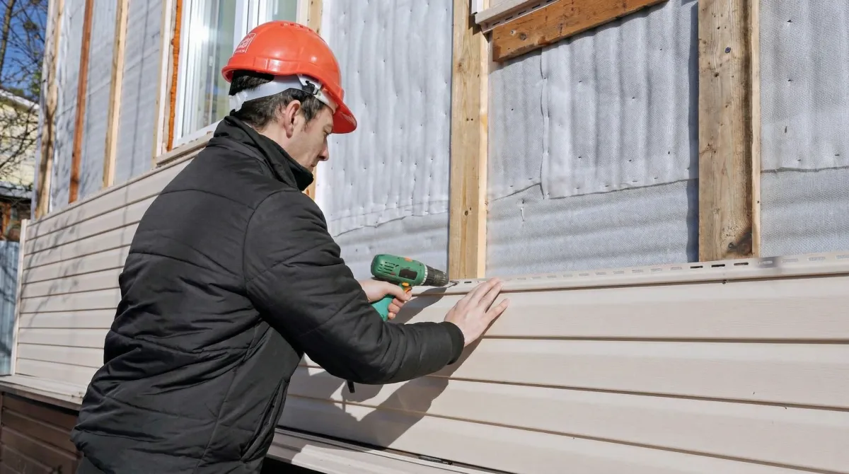 Siding replacement professional using a power drill to install new tan vinyl siding on a home exterior in San Francisco, CA